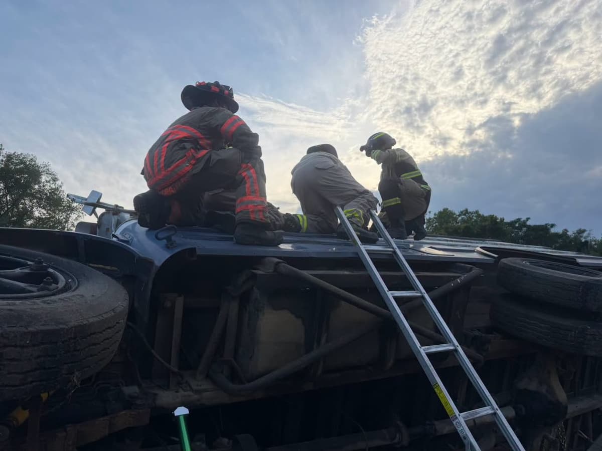 Firefighters using a ladder to reach the upper side of an overturned activity bus