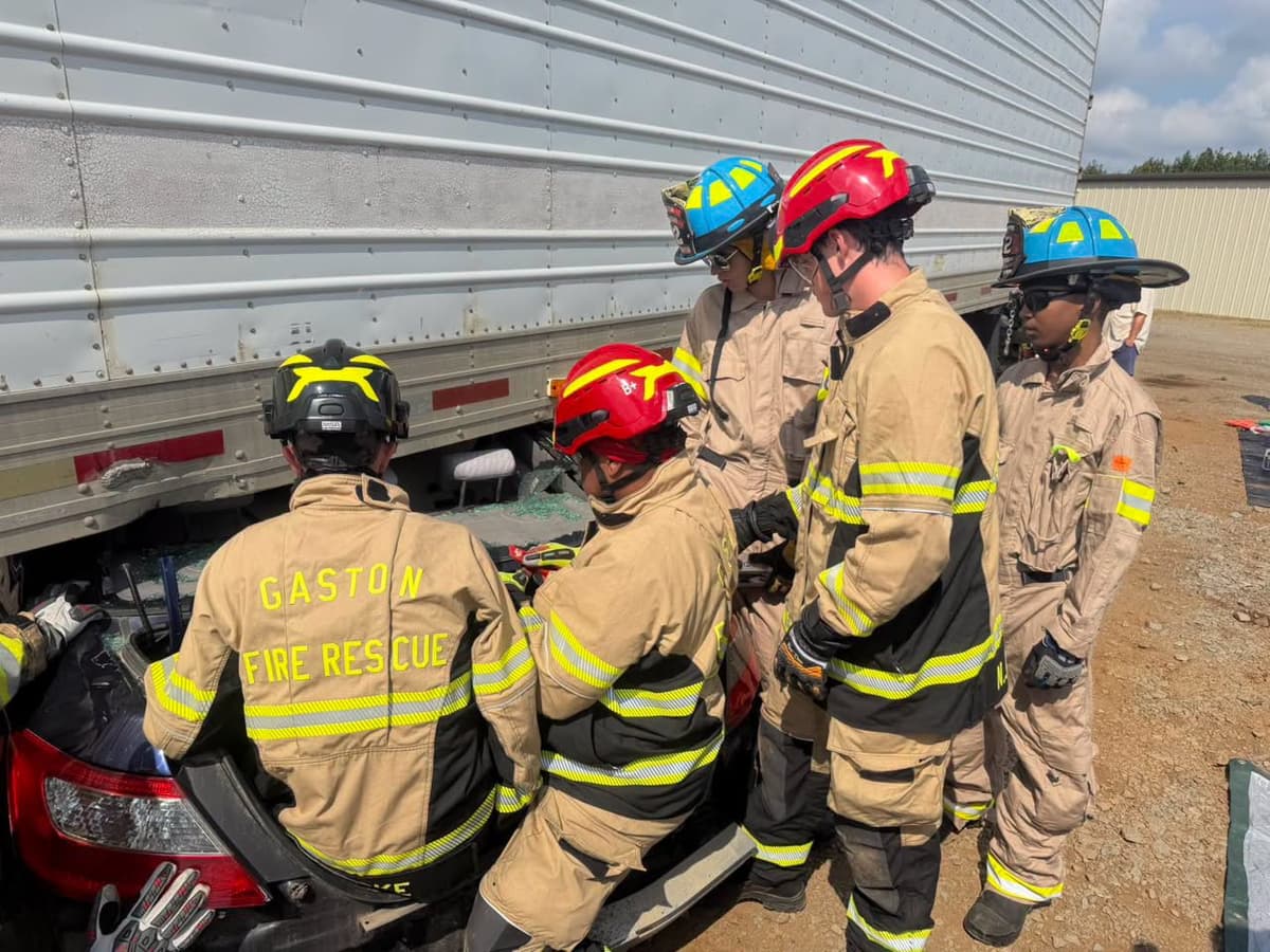 Gaston Fire and Rescue members working beside a passenger vehicle trapped beneath a tractor-trailer