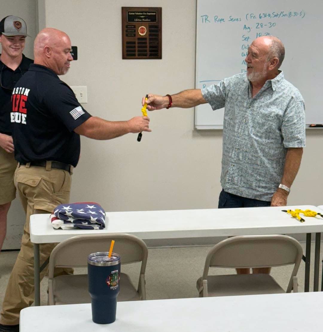 An instructor handing a yellow figure-eight knot to a Gaston member beside a table