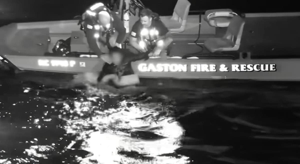 Nighttime image of rescue personnel leaning over the side of a Gaston Fire & Rescue boat toward a person in the water